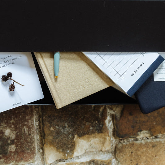 Stationery items including a pen, cards, and a notebook on a textured stone surface.