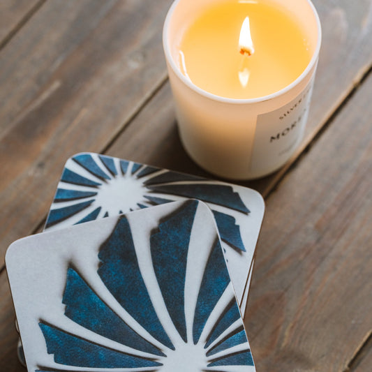 Coaster with blue and white design on a wooden surface with a lit candle.